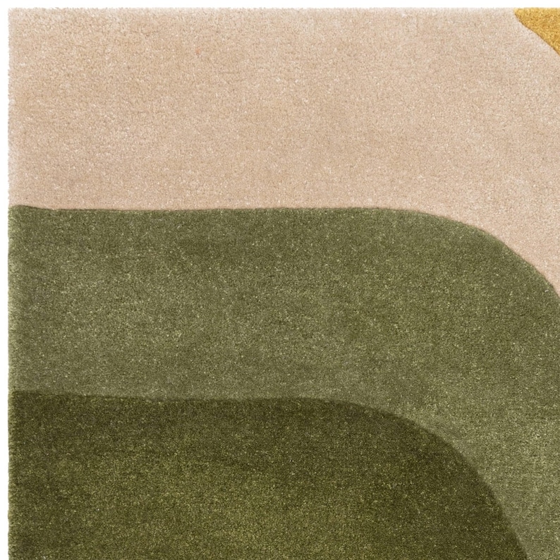 May include: A close-up of a rug with a geometric design. The rug features a beige top section, with two curved olive green sections below. A small section of yellow is visible in the upper right corner. The rug has a soft, textured appearance.
