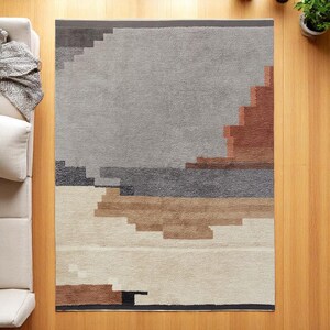 May include: A rectangular rug with a geometric pattern in grey, brown, and cream. The design includes a stepped pattern in the upper right corner and a border along the top edge. The rug is placed on a wooden floor.
