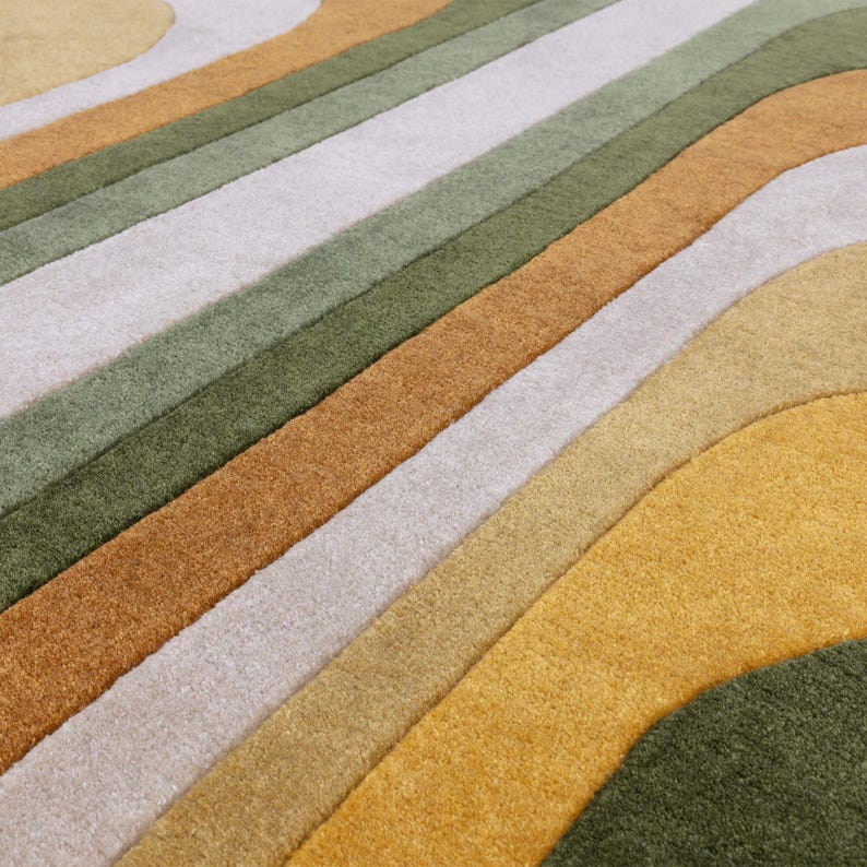 May include: A close-up of a colorful rug with a wavy striped pattern. The rug features a palette of warm colors, including shades of green, gold, and brown. The design is modern and abstract, with soft, textured fibers.