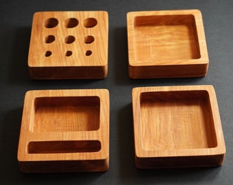 May include: A set of four wooden desk organisers. The organisers are made of light brown wood and have different compartments for pens, pencils, and other office supplies. The organisers are arranged in a square shape on a dark brown surface. The text "THIS IS Desk organiser" is at the bottom of the image. A brown circle with the text "HAND-MADE" is in the bottom right corner of the image.
