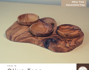 May include: A decorative olive wood tray with three small bowls. The tray is made of natural wood with a unique grain pattern. The bowls are perfect for serving snacks, dips, or condiments. The tray is hand-made and has a rustic, natural look.