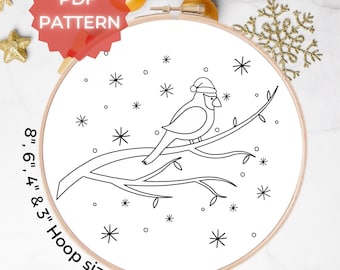 May include: A black and white embroidery hoop art featuring a cardinal wearing a Santa hat, perched on a branch with snowflakes. The text "PDF PATTERN" is in a red banner. Hoop sizes are 3", 4", 6", and 8".