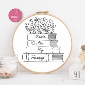 May include: A black and white embroidery hoop featuring a stack of books with the words "Books Are My Therapy." The design includes flowers and a heart. A pink circle with "Printable PDF" is in the upper left.