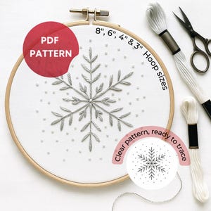 Op de afbeelding: Een sneeuwvlok borduurpatroon in een houten borduurring. Het ontwerp is gestikt met zilver garen en bevat kleine witte kralen. De tekst "PDF PATTERN" staat in een rode cirkel. Hoepelmaten zijn 20cm, 15cm, 10cm en 7.6cm. De tekst "Clear pattern, ready to trace" is ook inbegrepen.