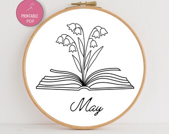 May include: A black and white embroidery hoop featuring a floral design emerging from an open book. The word "May" is scripted below the book. A pink circle with the words "Printable PDF" is in the upper left corner.