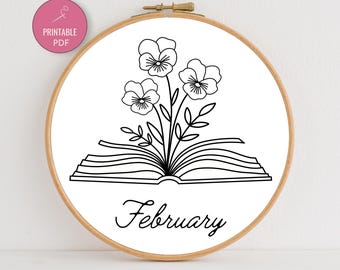 May include: A wooden embroidery hoop with a white fabric featuring a black line drawing of flowers emerging from an open book. The word "February" is written below the book in a cursive font. A pink circle with the words "Printable PDF" is in the upper left corner.