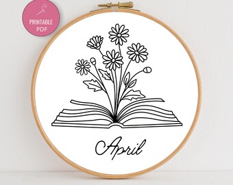 May include: A black and white embroidery hoop featuring a floral design emerging from an open book. The word "April" is written in cursive below the book. A pink circle with the words "PRINTABLE PDF" is in the upper left corner.