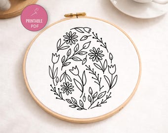 May include: A floral embroidery hoop featuring a black line art design of flowers and leaves arranged in an egg shape. The design is on white fabric, held in a wooden hoop. A pink circle with the text "Printable PDF" is visible.