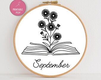 May include: A wooden embroidery hoop with a white background featuring a black line drawing of a book with flowers growing from it. The word "September" is written below the book in cursive. A pink circle with the words "Printable PDF" is in the upper left.