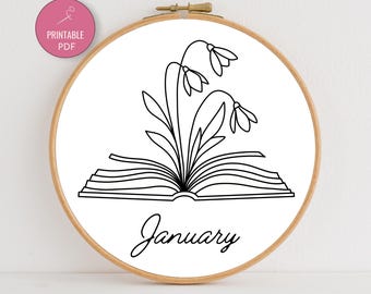 May include: A wooden embroidery hoop with a white fabric featuring a black line drawing of a book with flowers and the word "January". A pink circle with the words "PRINTABLE PDF" is in the upper left corner.