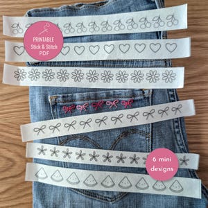 Può includere: Sei strisce di tessuto bianco con motivi a linee nere di ciliegie, cuori, margherite, fiocchi, fiori e fette di anguria. Un'etichetta rosa riporta la scritta PRINTABLE Stick & Stitch PDF e 6 mini designs su un tessuto denim blu.