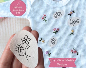 May include: A light blue baby onesie with a waffle knit texture, adorned with embroidered flowers in pink, yellow, and green. The image also shows a hand holding a sticker with a black floral design and the text "Printable Stick & Stitch PDF" and "Tiny Mix & Match Designs".
