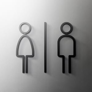 Puede incluir: Señales de baño en blanco y negro con una figura de palo que representa a una mujer a la izquierda y una figura de palo que representa a un hombre a la derecha. Una línea vertical separa las dos figuras.
