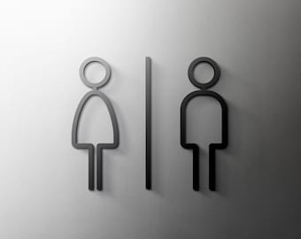 May include: Black and white restroom signs with a stick figure representing a woman on the left and a stick figure representing a man on the right. A vertical line separates the two figures.