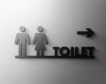 May include: Black and white sign with a male and female symbol, an arrow pointing to the right, and the word "TOILET" in black letters.