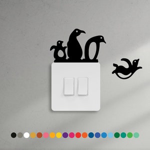 Puede incluir: Un interruptor de luz blanco con dos botones de palanca y una pegatina negra de una familia de pingüinos encima. Los pingüinos están en fila, con el pingüino más grande en el medio y dos pingüinos más pequeños a cada lado. La pegatina está en una pared gris claro.