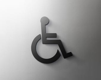 Puede incluir: Un símbolo negro de silla de ruedas, un signo universal de accesibilidad, se representa sobre un fondo gris degradado. El símbolo es una representación estilizada de una persona en silla de ruedas, con una rueda circular y una figura sentada.