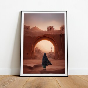 May include: A person wearing a dark blue robe walks through an archway in a desert landscape. The archway is made of red sandstone and leads to a small town in the distance. The sky is a soft orange and pink.