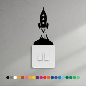 May include: A black and white rocket ship decal on a white light switch cover. The rocket is taking off with flames coming out of the bottom.