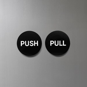 May include: Two black round signs with white text. The sign on the left says "PUSH" and the sign on the right says "PULL".