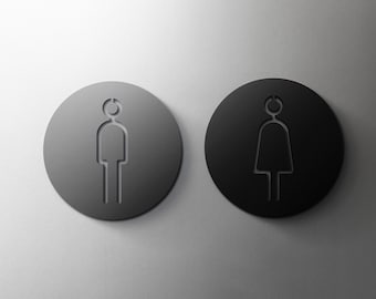 May include: Two round black signs with white outlines of a person and a woman, indicating a restroom.