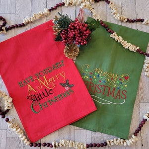 May include: Two red and green kitchen towels with embroidered Christmas sayings. The red towel says "Have Yourself A Merry Little Christmas" and the green towel says "Merry Christmas" with a string of lights design.