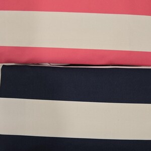 May include: Close-up of striped fabric in various colors. The fabric features wide horizontal stripes in blue, pink, navy, and green, alternating with white stripes. The texture appears to be a tightly woven canvas or similar material.