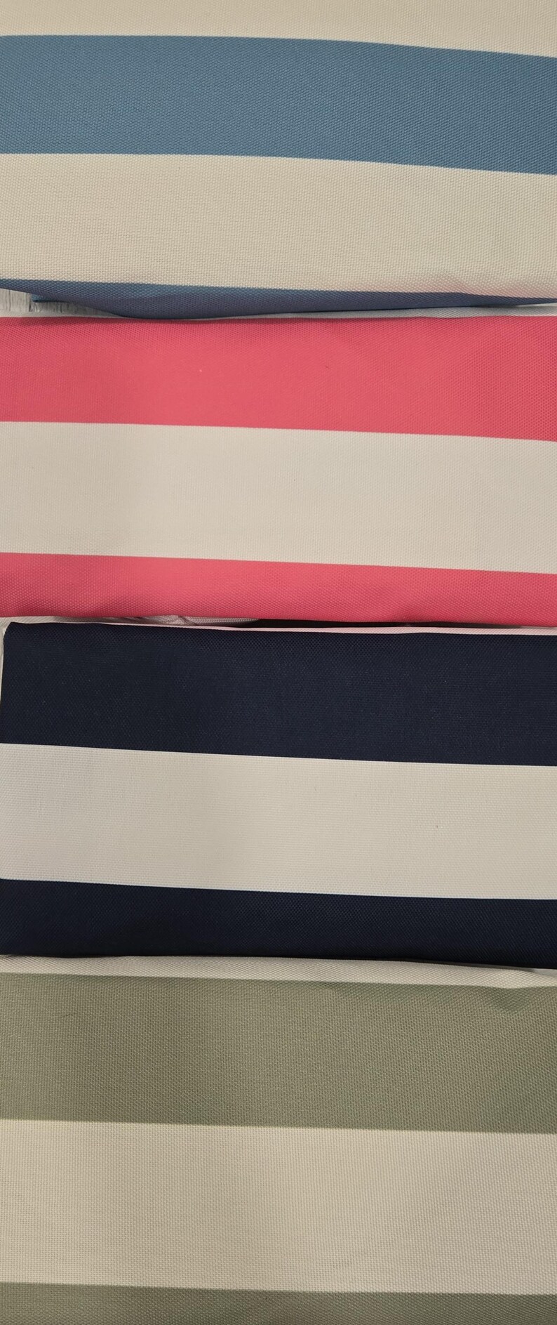 May include: Close-up of striped fabric in various colors. The fabric features wide horizontal stripes in blue, pink, navy, and green, alternating with white stripes. The texture appears to be a tightly woven canvas or similar material.