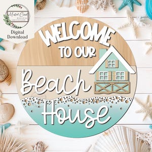 May include: Welcome to our beach house sign with a light blue beach house graphic, white text, and a brown wood background.