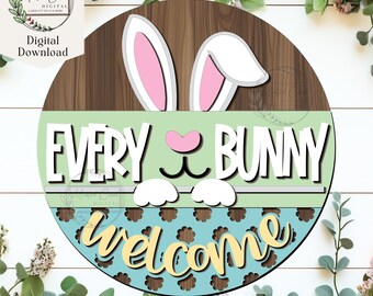 Pode incluir: Um sinal redondo de madeira com um rosto de coelho e o texto "Every Bunny Welcome" em um esquema de cores verde, branco e azul. O coelho tem orelhas cor-de-rosa e um nariz cor-de-rosa.