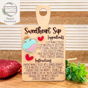 Puede incluir: Un letrero de madera con forma de tabla de cortar con el texto "Sweetheart Sip" y una lista de ingredientes e instrucciones para una bebida. Los ingredientes incluyen besos a la luz de la luna, susurros de afecto, gotas eternas de sol, burbujas de risa, serenata de cuerdas del corazón y chispas de polvo de estrellas. Las instrucciones dicen que se combinen los ingredientes con recuerdos compartidos, se revuelva con susurros de afecto, se añadan gotas eternas de sol para calentar, se espolvoreen burbujas de risa para la alegría, se mezcle con serenata de cuerdas del corazón y se termine con una pizca de chispas de polvo de estrellas.
