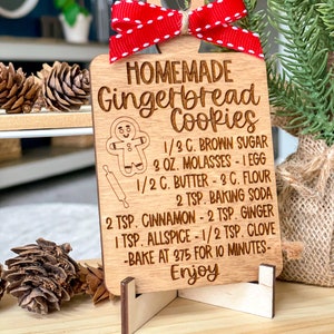 May include: A wooden gingerbread cookie recipe ornament with a gingerbread man illustration and the text "HOMEMADE Gingerbread Cookies 1/3 C. BROWN SUGAR 3 OZ. MOLASSES - 1 EGG 1/2 C. BUTTER - 3 C. FLOUR 2 TSP. BAKING SODA 2 TSP. CINNAMON - 2 TSP. GINGER 1 TSP. ALLSPICE - 1/2 TSP. CLOVE -BAKE AT 375 FOR 10 MINUTES- Enjoy".