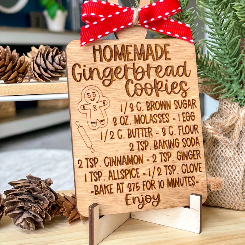 May include: A wooden gingerbread cookie recipe ornament with a gingerbread man illustration and the text "HOMEMADE Gingerbread Cookies 1/3 C. BROWN SUGAR 3 OZ. MOLASSES - 1 EGG 1/2 C. BUTTER - 3 C. FLOUR 2 TSP. BAKING SODA 2 TSP. CINNAMON - 2 TSP. GINGER 1 TSP. ALLSPICE - 1/2 TSP. CLOVE -BAKE AT 375 FOR 10 MINUTES- Enjoy".