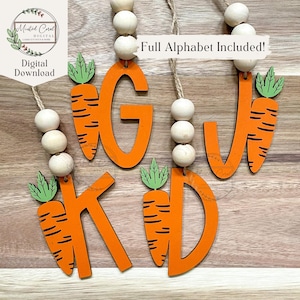 May include: Wooden letters in orange, with a carrot design, are strung with wooden beads. The letters are G, W, K, and D. Each letter has a carrot attached, with green leaves and orange carrots. The text "Full Alphabet Included!" is visible.