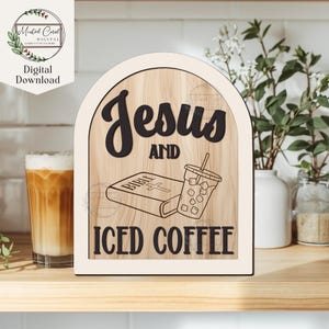 May include: Wooden sign with the words "Jesus AND ICED COFFEE" in black lettering. The sign features a Bible and a cup of iced coffee. The sign has a light wood grain background and a white border. A glass of iced coffee is in the background.
