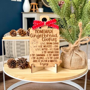 May include: Wooden gingerbread cookie recipe ornament with a red ribbon. The ornament has a gingerbread man illustration and the text "HOMEMADE Gingerbread Cookies" and the recipe ingredients and instructions.
