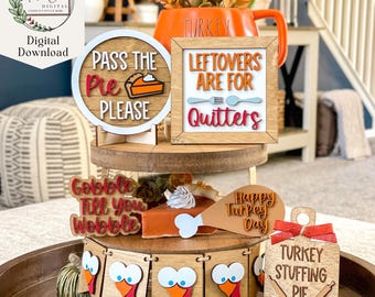 May include: A tiered tray decorated for Thanksgiving with a variety of wooden signs. The signs feature Thanksgiving-themed phrases like "Pass the Pie Please", "Leftovers are for Quitters", "Gobble Till You Wobble", "Happy Turkey Day", and "Turkey Stuffing Pie Oh My!".