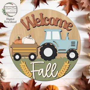 May include: A round wooden sign with a light brown background features the words "Welcome Fall" and a light blue tractor pulling a wagon with pumpkins. The sign is decorated with fall leaves and wheat.