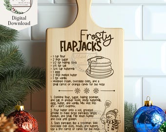 May include: A wooden cutting board with a recipe for "Frosty Flapjacks" engraved on it. The recipe includes ingredients like flour, sugar, baking soda, and buttermilk. The board also features a snowman illustration and a stack of pancakes.