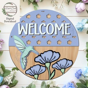 May include: A round wooden welcome sign with a light blue top section featuring flower cutouts and the word "WELCOME" in white. A hummingbird and blue flowers decorate the bottom half. The sign is a digital download.
