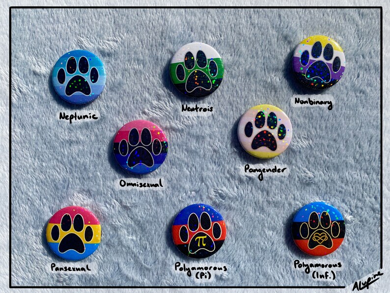 May include: A collection of nine round buttons with paw print designs, each featuring a different color scheme and text label. The buttons represent various LGBTQ+ identities, including "Neptunic," "Omnisexual," and "Nonbinary."