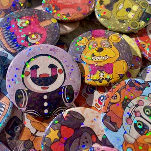 May include: A collection of round, colorful buttons featuring cartoon characters with glittery, holographic accents. The buttons showcase various designs, including a puppet-like figure and a yellow bear with a purple bow tie. The buttons are likely fan-made merchandise.