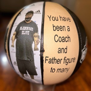 Op de afbeelding: Een basketbal met een zwart-wit ontwerp. Aan de ene kant is een foto van een man die twee trofee&euml;n vasthoudt. Aan de andere kant staat de tekst "You have been a Coach and Father figure to many".