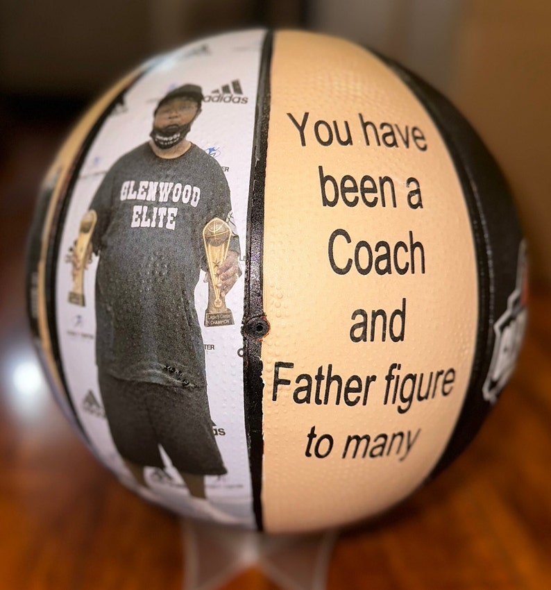 Op de afbeelding: Een basketbal met een zwart-wit ontwerp. Aan de ene kant is een foto van een man die twee trofee&euml;n vasthoudt. Aan de andere kant staat de tekst "You have been a Coach and Father figure to many".