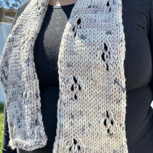 Peut inclure: Une écharpe tricotée avec un motif moucheté blanc et gris et des trous noirs dans tout le tissu.