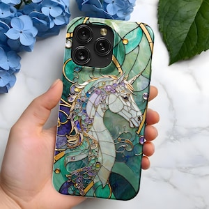 May include: A white unicorn with a green, blue, and purple stained glass design on a phone case. The phone case has a gold trim and a clear camera lens.