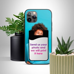 Op de afbeelding: Een zwarte telefoonhoes met een blauwe achtergrond en een foto van een gezicht dat uit een zwarte kaarthouder steekt. De kaarthouder heeft de tekst "Stuur ons je foto en we printen hem hier".