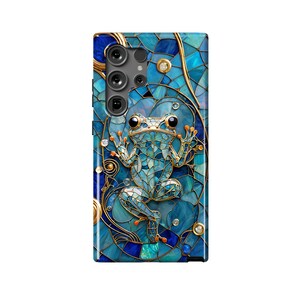 Peut inclure: Une coque de t&eacute;l&eacute;phone bleue et dor&eacute;e avec un motif en mosa&iuml;que repr&eacute;sentant une grenouille. La coque a une d&eacute;coupe pour l'objectif de l'appareil photo.