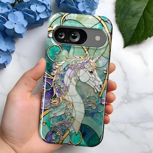 May include: A phone case with a stained glass design featuring a white unicorn with a gold horn and blue, green, and purple accents. The case has a camera cutout and a clear back.