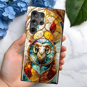 May include: A phone case with a stained glass design featuring a ram's head in the centre. The case is decorated with gold, red, blue and green colours.